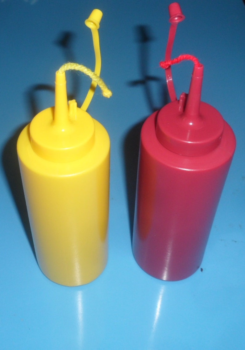 May include: Two plastic condiment bottles with squeeze tops and twist-on lids. The bottle on the left is yellow and the bottle on the right is red.