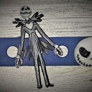 May include: A black and white striped figure of Jack Skellington from the Nightmare Before Christmas movie. The figure is standing on a blue background with a white background behind it.
