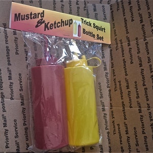 May include: Two plastic squeeze bottles, one red and one yellow, labeled "Mustard & Ketchup Trick Squirt Bottle Set".