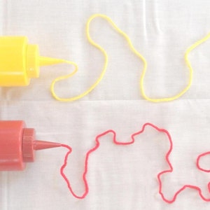 May include: Two plastic squeeze bottles, one yellow and one red, with a red and yellow string coming out of the spout of each bottle.