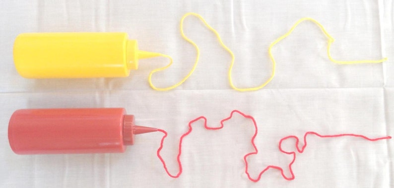 May include: Two plastic squeeze bottles, one yellow and one red, with a red and yellow string coming out of the spout of each bottle.