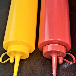 May include: Two plastic condiment bottles with squeeze tops. The bottle on the left is yellow and the bottle on the right is red.