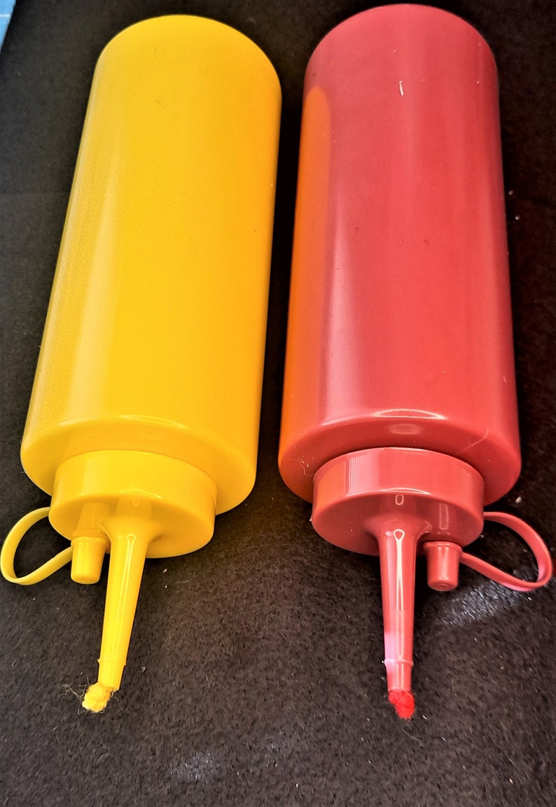 May include: Two plastic condiment bottles with squeeze tops. The bottle on the left is yellow and the bottle on the right is red.