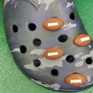 May include: A close-up of a blue and gray camouflage shoe with five brown football-shaped charms attached to it.