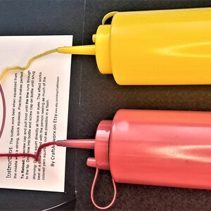 May include: A red and yellow plastic ketchup and mustard squeeze bottle set with a target practice game. The game includes a target with concentric circles and instructions for playing the game. The text on the target reads "Startled Jump" and "Conquered by Squeew".