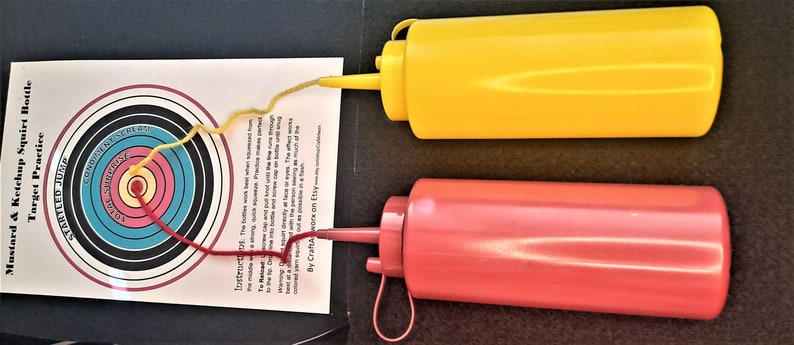 May include: A red and yellow plastic ketchup and mustard squeeze bottle set with a target practice game. The game includes a target with concentric circles and instructions for playing the game. The text on the target reads "Startled Jump" and "Conquered by Squeew".
