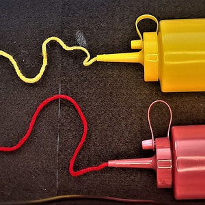 May include: Two condiment bottles, one yellow and one red, with a squiggle of yellow sauce coming out of the yellow bottle and a squiggle of red sauce coming out of the red bottle.