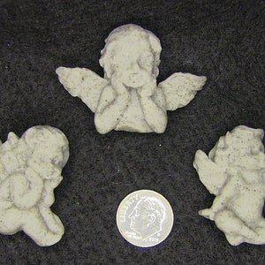 May include: Three small, gray, concrete cherub figurines. The cherubs are in different poses, with one sitting with its hands clasped in front of its face, one sitting with its hands clasped behind its back, and one sitting with its hands clasped in front of its chest. The cherubs are all about 2 inches tall.