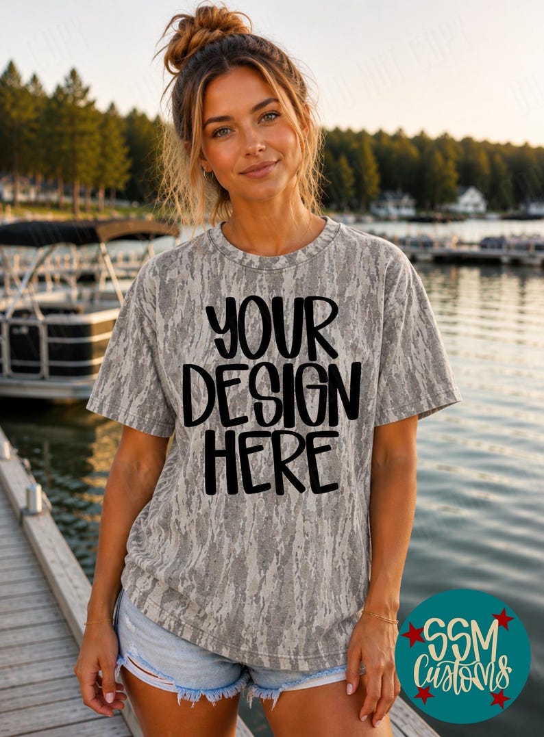 May include: A short-sleeved t-shirt with a grey and white camouflage pattern. The front of the shirt features the black text "YOUR DESIGN HERE" in a bold, rounded font. The garment has a crew neckline and a relaxed fit, constructed from fabric.