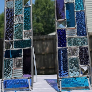 May include: Two stained glass panels with a rectangular shape. The panels feature a mosaic of blue, teal, and purple glass pieces, framed in silver metal. The panels are labeled "A" and "B" with the number "10" below panel "A".