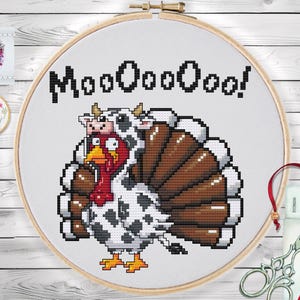 May include: Cross-stitch embroidery in a wooden hoop features a turkey wearing a cow costume, with the text "Moooooo!". The turkey has a red head and brown tail feathers. The cow costume is white with black spots. A fun, whimsical design.