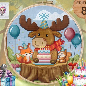 May include: Cross-stitch hoop art featuring a moose, fox, and squirrel celebrating a birthday. The moose wears a party hat and scarf, holding a cake. Balloons and a birthday cake are also present. The artwork is set in a forest scene.