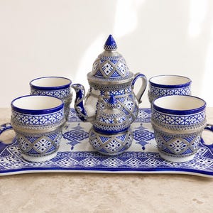 Peut inclure: Un service à thé en céramique comprenant une théière, un sucrier avec couvercle et quatre tasses disposés sur un plateau rectangulaire. Chaque pièce est ornée d'un motif géométrique bleu et blanc avec des détails métalliques argentés.