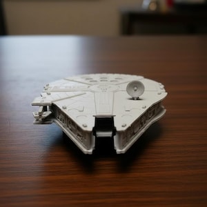 Può includere: Un modello grigio chiaro dell'astronave Millennium Falcon. Il modello presenta pannelli dettagliati, un radar circolare e un vano di attracco rettangolare. L'astronave è un oggetto popolare del franchise di Star Wars.