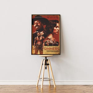May include: A framed movie poster for "Sinners" featuring Michael B. Jordan. The poster has a red and brown color scheme with images of the actors. The poster is displayed on a wooden stool with a round top and three wooden legs.