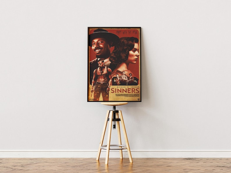 May include: A framed movie poster for "Sinners" featuring Michael B. Jordan. The poster has a red and brown color scheme with images of the actors. The poster is displayed on a wooden stool with a round top and three wooden legs.