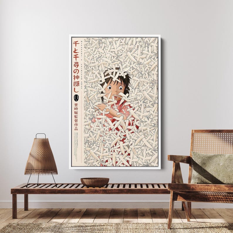 May include: Framed art print featuring a scene from the animated film "Spirited Away." The artwork depicts a young girl in a red outfit surrounded by white figures. Japanese text is visible on the left side of the print.