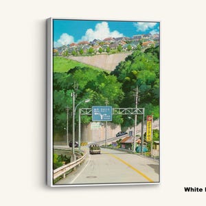 May include: White framed canvas art print featuring a scenic road leading through a lush green landscape. The artwork depicts a road sign, buildings, and a blue sky with clouds. A bus and cars are on the road.