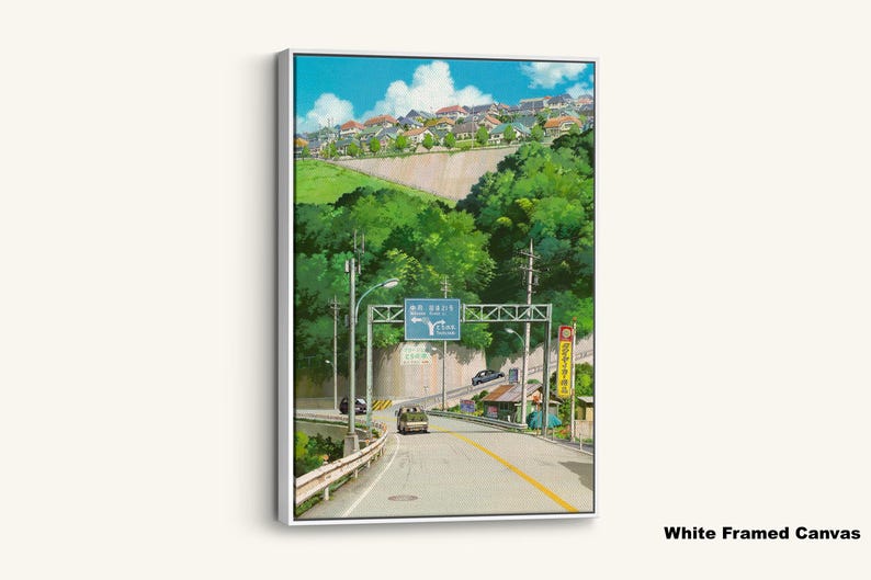 May include: White framed canvas art print featuring a scenic road leading through a lush green landscape. The artwork depicts a road sign, buildings, and a blue sky with clouds. A bus and cars are on the road.