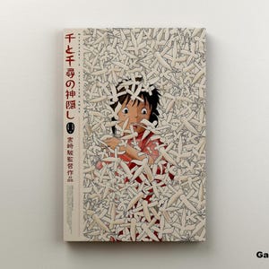 May include: Canvas art print featuring a scene from the animated film "Spirited Away." The artwork depicts a character surrounded by white figures, with Japanese text on the left side. The canvas is mounted on a white wall.