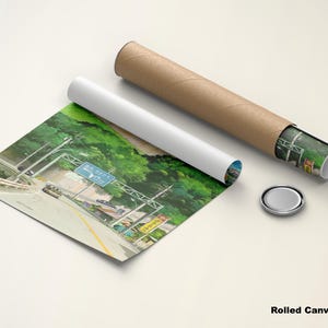 May include: A rolled canvas poster featuring a scenic highway view with lush green trees and a blue road sign. The poster is partially unrolled, with a white tube and a brown cardboard tube next to it. A silver cap is also present.