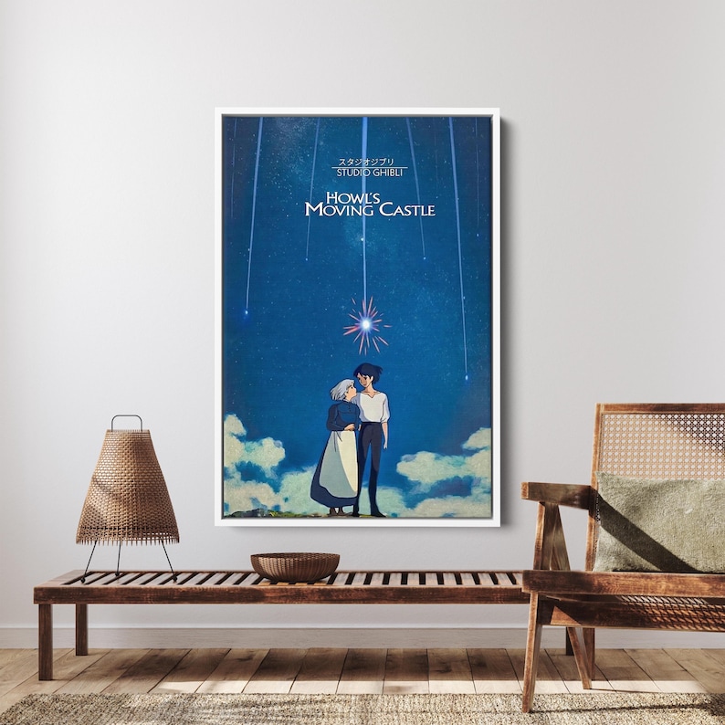 K&ouml;nnte beinhalten: Ein gerahmtes Poster mit einer Szene aus "Das wandelnde Schloss" mit sternenklarem Nachthimmel und zwei sich umarmenden Figuren. Das Poster tr&auml;gt den Filmtitel und den Namen des Studios in wei&szlig;er Schrift. Das Kunstwerk wird auf einer Holzbank pr&auml;sentiert.