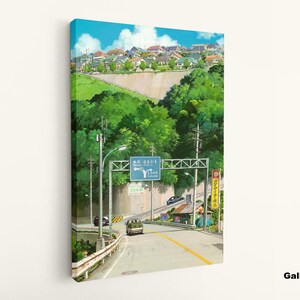 May include: Canvas art print of a road scene with a blue sky and a town in the background. The artwork features a road with a yellow center line, green trees, and a sign with Japanese text. The canvas is mounted on a white wall.