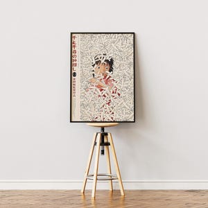 May include: Framed poster featuring a character from an animated film, surrounded by a pattern of white shapes. The poster has Japanese text and is displayed on a wooden and metal adjustable stool against a white wall.