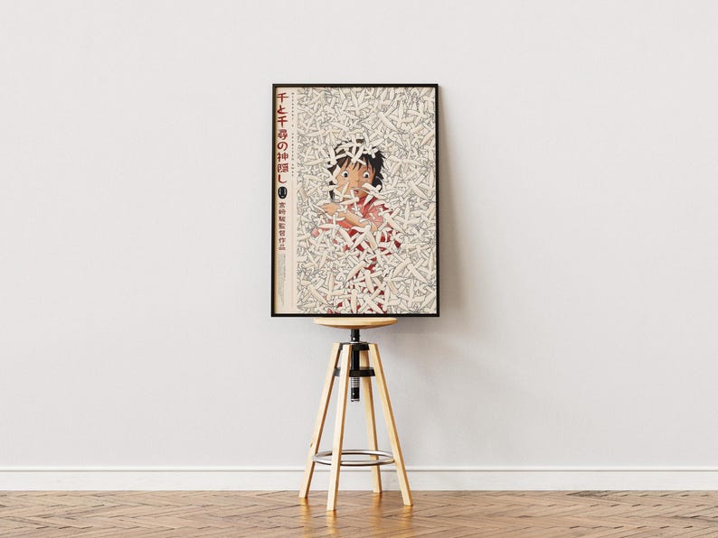 May include: Framed poster featuring a character from an animated film, surrounded by a pattern of white shapes. The poster has Japanese text and is displayed on a wooden and metal adjustable stool against a white wall.