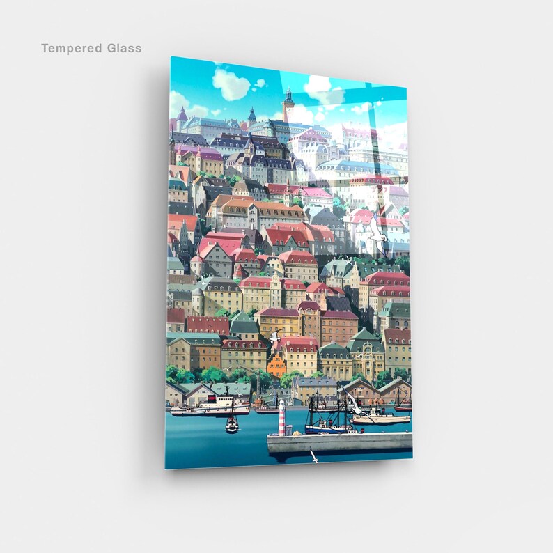 May include: Tempered glass art print featuring a colorful illustration of a coastal town with buildings of various colors and architectural styles. Boats and a lighthouse are visible in the harbor under a blue sky.