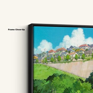 May include: Close-up of a framed canvas print featuring a vibrant illustration of a hillside town under a bright blue sky with fluffy white clouds. The artwork showcases houses with various colored roofs and lush green foliage.