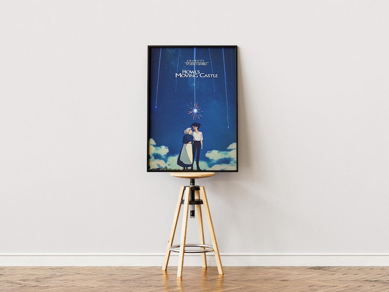 K&ouml;nnte beinhalten: Ein gerahmtes Poster mit dem Anime-Film "Das wandelnde Schloss". Das Kunstwerk zeigt zwei Figuren, die sich unter einem Sternenhimmel umarmen. Das Poster wird auf einem verstellbaren Hocker aus Holz und Metall vor einer wei&szlig;en Wand pr&auml;sentiert.