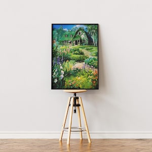 May include: A framed print of a picturesque garden scene. The artwork depicts a house with a green roof surrounded by lush greenery, colorful flowers, and a winding path. The print is displayed on a wooden stool.