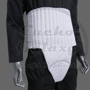 May include: A white padded waist belt with vertical stitching and a matching white groin guard piece, worn over a black long-sleeved shirt and black trousers. The garment features a clean, segmented design with a smooth, matte finish throughout.