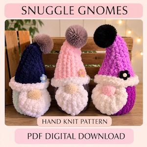Pode incluir: Três gnomos de pelúcia feitos à mão com gorros de lã texturizada, pompons e barbas brancas. O gnomo da esquerda tem um gorro azul-marinho, o central um rosa e o da direita um roxo. Cada um tem uma pequena flor. Texto: SNUGGLE GNOMES HAND KNIT PATTERN PDF DIGITAL DOWNLOAD.
