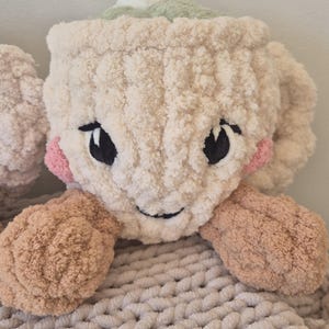 Pu&ograve; includere: Un peluche a forma di tazza lavorato all'uncinetto color crema con una consistenza morbida e soffice. Presenta occhi neri ricamati, un piccolo sorriso, guance circolari rosa e due braccia color marrone chiaro sui lati. Parte superiore verde chiaro.
