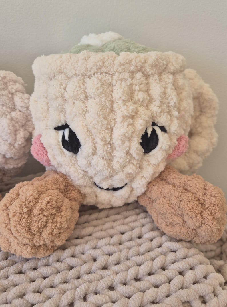 Pu&ograve; includere: Un peluche a forma di tazza lavorato all'uncinetto color crema con una consistenza morbida e soffice. Presenta occhi neri ricamati, un piccolo sorriso, guance circolari rosa e due braccia color marrone chiaro sui lati. Parte superiore verde chiaro.