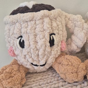 Pu&ograve; includere: Un peluche lavorato all'uncinetto a forma di tazza color crema, con una parte superiore marrone scuro, una stella bianca, occhi e bocca ricamati in nero e guance rosa. La tazza presenta due braccia color marrone chiaro sui lati.