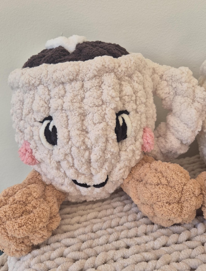 Pu&ograve; includere: Un peluche lavorato all'uncinetto a forma di tazza color crema, con una parte superiore marrone scuro, una stella bianca, occhi e bocca ricamati in nero e guance rosa. La tazza presenta due braccia color marrone chiaro sui lati.