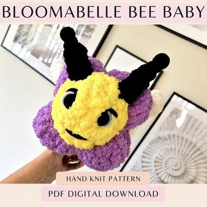 Könnte beinhalten: Ein Plüschtier in Form einer Biene mit gelbem Gesicht, schwarzen Fühlern und violetten Blütenblättern um den Kopf. Der Text BLOOMABELLE BEE BABY, HAND KNIT PATTERN und PDF DIGITAL DOWNLOAD ist in schwarzen Buchstaben auf dem Bild gedruckt.