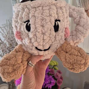 Pu&ograve; includere: Un peluche lavorato all'uncinetto a forma di tazza color crema, con una parte superiore marrone scuro, un accento di schiuma bianca e braccia color marrone chiaro. La tazza presenta occhi neri ricamati, un sorriso nero e guance rosa.