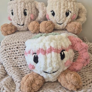 Pu&ograve; includere: Tre peluche a forma di tazza realizzati in morbido filato spesso. Due tazze sono color crema con la parte superiore marrone, mentre la terza &egrave; bianca con strisce rosa e la parte superiore verde. Ogni tazza presenta occhi neri ricamati e guance rosa.