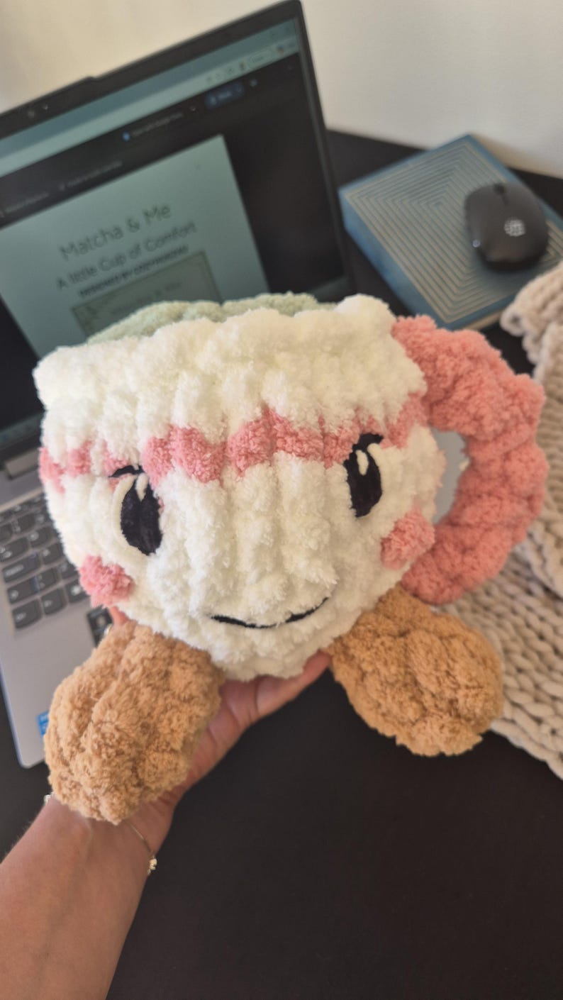 Pu&ograve; includere: Un peluche all'uncinetto a forma di tazza con corpo bianco, bordo a righe rosa e manico rosa. Presenta occhi ricamati neri, un sorriso nero e guance rosa. La base &egrave; color marrone chiaro con due piccoli piedi arrotondati sul fondo.