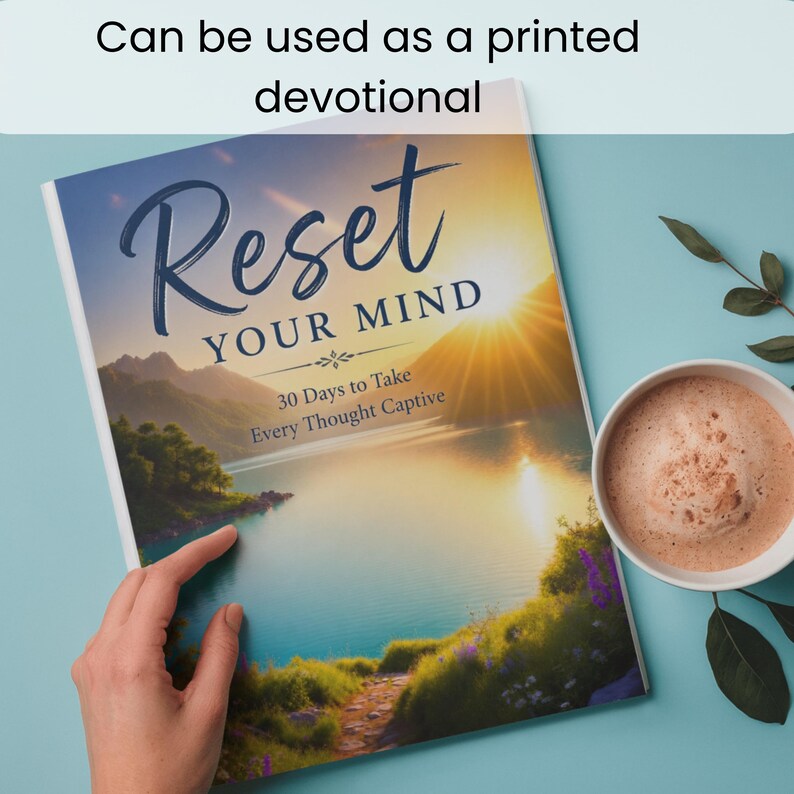 Op de afbeelding: Een boek getiteld Reset YOUR MIND 30 Days to Take Every Thought Captive met een landschapscover met een meer, bergen en een zonsondergang. Het boek ligt naast een witte mok gevuld met een lichtbruine drank en groene bladeren.