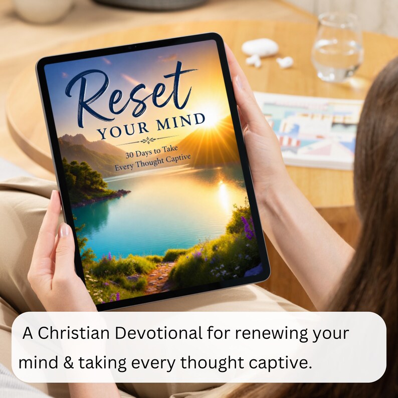 Op de afbeelding: Een digitale tablet met een boekomslag getiteld Reset YOUR MIND 30 Days to Take Every Thought Captive. De omslag toont een levendige zonsondergang boven een kalm meer, omringd door bergen en weelderig groen met paarse bloemen op de voorgrond.
