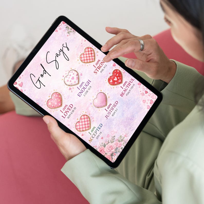 Op de afbeelding: Een digitaal tabletscherm toont een roze aquarelachtergrond met de tekst God Says en zes hartvormige koekjes. Elk koekje bevat een positieve affirmatie en een bijbelversverwijzing, waaronder I am STRONG, ENOUGH, LOVED, BEAUTIFUL, JUSTIFIED en ACCEPTED.