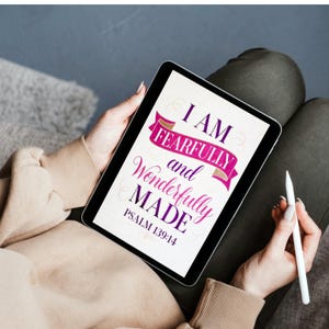 May include: A digital tablet displaying the text I AM FEARFULLY and Wonderfully MADE PSALM 139:14 in purple and pink lettering. The design features a pink ribbon graphic behind the word FEARFULLY and thin decorative swirls on a white background.