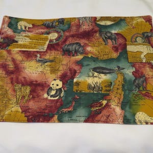 May include: A colorful fabric placemat with a vintage world map design. The map features various animals, including a panda, tiger, rhinoceros, and elephant. The placemat is a great addition to any dining table.