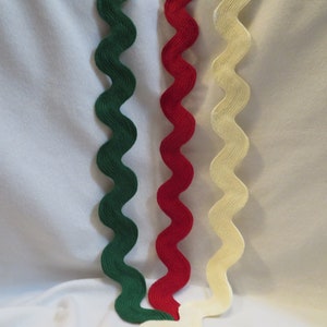 May include: Three strips of wavy rickrack trim arranged vertically. The trim is available in three distinct colors: a deep forest green, a vibrant crimson red, and a soft off-white cream. Each strip features a consistent undulating pattern.