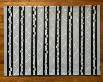 May include: Rectangular gray fabric with a repeating pattern of vertical black and white wavy lines. The design creates a modern, minimalist aesthetic. The fabric is likely used for home decor, such as a rug or placemat.